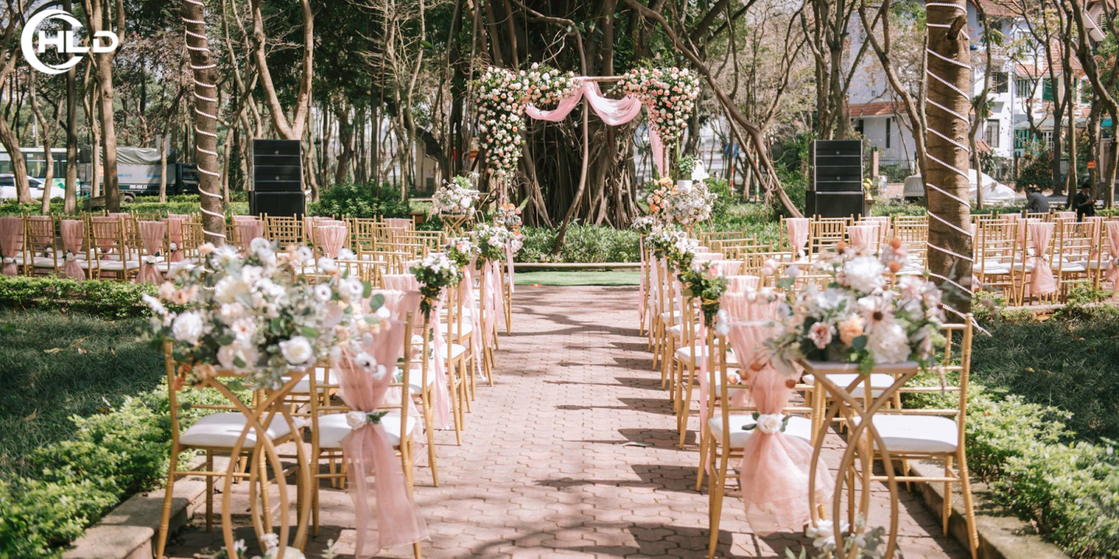 Backdrop Đám Cưới Ngoài Trời Phong Cách Châu Âu Đẹp Xuất Sắc  Một đám cưới ngoài trời luôn mang đến cảm giác lãng mạn, tự do và đầy cảm xúc. Khi không gian thiên nhiên được kết hợp cùng nghệ thuật trang trí tinh tế, buổi lễ cưới trở thành một khung cảnh như bước ra từ câu chuyện cổ tích. Trong đó, backdrop đám cưới ngoài trời chính là chi tiết quan trọng tạo nên linh hồn của toàn bộ không gian lễ cưới.  Nếu sân khấu là nơi cô dâu chú rể thực hiện những nghi thức thiêng liêng, thì backdrop đám cưới ngoài trời chính là phông nền giúp khoảnh khắc ấy trở nên hoàn hảo hơn. Một thiết kế đẹp không chỉ tạo điểm nhấn nổi bật cho buổi lễ mà còn giúp mọi bức ảnh cưới trở nên sang trọng và đầy cảm xúc.  Trong những năm gần đây, xu hướng backdrop đám cưới ngoài trời phong cách châu Âu đang được nhiều cặp đôi yêu thích. Phong cách này mang đến vẻ đẹp tinh tế, thanh lịch nhưng vẫn rất lãng mạn. Những chi tiết như hoa tươi, khung vòm, rèm lụa mềm mại hay ánh đèn vàng ấm áp giúp không gian lễ cưới trở nên nhẹ nhàng và đầy cảm xúc.  Khi kết hợp cùng concept Trang trí đám cưới tổng thể, một backdrop đám cưới ngoài trời đẹp sẽ giúp toàn bộ buổi tiệc trở nên sang trọng, hài hòa và đáng nhớ hơn bao giờ hết.  Backdrop Đám Cưới Ngoài Trời – Linh Hồn Của Không Gian Lễ Cưới Lãng Mạn  Trong một buổi lễ cưới ngoài trời, không gian thiên nhiên vốn đã rất đẹp, nhưng để tạo nên một tổng thể thật sự ấn tượng thì yếu tố trang trí đóng vai trò vô cùng quan trọng. Trong đó, backdrop đám cưới ngoài trời chính là chi tiết thu hút mọi ánh nhìn và trở thành trung tâm của buổi lễ.  Khi cô dâu bước vào lễ đường trong tiếng nhạc du dương, mọi ánh mắt đều hướng về khu vực sân khấu nơi diễn ra nghi thức trao lời thề nguyện. Lúc này, backdrop đám cưới ngoài trời không chỉ là phông nền trang trí mà còn là nơi lưu giữ những khoảnh khắc cảm xúc nhất của cặp đôi.  Một backdrop đám cưới ngoài trời được thiết kế tinh tế sẽ giúp không gian buổi lễ trở nên sang trọng và hài hòa với thiên nhiên xung quanh. Ánh nắng nhẹ, những cơn gió thoảng qua cùng hoa tươi và vải lụa tạo nên một khung cảnh vừa lãng mạn vừa trang nhã.  Trong nghệ thuật Trang trí đám cưới, backdrop đóng vai trò như tâm điểm của toàn bộ concept. Khi thiết kế backdrop phù hợp với chủ đề buổi lễ, mọi chi tiết xung quanh như lối đi hoa, bàn gallery hay khu vực tiếp khách cũng trở nên đồng bộ và đẹp mắt hơn.  Chính vì vậy, nhiều cặp đôi hiện nay sẵn sàng đầu tư cho một backdrop đám cưới ngoài trời thật sự ấn tượng để biến ngày cưới của mình trở thành một kỷ niệm đáng nhớ.  Vẻ Đẹp Tinh Tế Của Backdrop Đám Cưới Ngoài Trời Phong Cách Châu Âu  Phong cách châu Âu trong Trang trí đám cưới luôn mang đến cảm giác thanh lịch và sang trọng. Không quá cầu kỳ nhưng lại vô cùng tinh tế, phong cách này chú trọng vào sự hài hòa của màu sắc, chất liệu và ánh sáng.  Một backdrop đám cưới ngoài trời mang phong cách châu Âu thường sử dụng những gam màu nhẹ nhàng như trắng, kem, pastel hoặc xanh lá. Những màu sắc này giúp tôn lên vẻ đẹp tự nhiên của không gian ngoài trời và tạo cảm giác nhẹ nhàng, lãng mạn.  Bên cạnh màu sắc, chất liệu cũng đóng vai trò quan trọng trong thiết kế backdrop đám cưới ngoài trời. Những tấm rèm lụa mềm mại, khung vòm kim loại thanh mảnh hay các chi tiết gỗ tự nhiên đều góp phần tạo nên vẻ đẹp tinh tế và sang trọng.  Hoa tươi cũng là yếu tố không thể thiếu trong Trang trí đám cưới phong cách châu Âu. Những cụm hoa được sắp xếp tự nhiên trên backdrop đám cưới ngoài trời giúp không gian buổi lễ trở nên mềm mại và lãng mạn hơn. Khi ánh hoàng hôn buông xuống, toàn bộ khung cảnh sẽ trở nên lung linh và đầy cảm xúc.  Nhờ sự kết hợp hài hòa giữa thiên nhiên và nghệ thuật trang trí, một backdrop đám cưới ngoài trời phong cách châu Âu luôn mang đến cảm giác vừa sang trọng vừa gần gũi, khiến buổi lễ cưới trở thành khoảnh khắc khó quên.  Vì Sao Backdrop Đám Cưới Ngoài Trời Được Nhiều Cặp Đôi Yêu Thích  Trong xu hướng Trang trí đám cưới hiện đại, các cặp đôi ngày càng yêu thích những không gian cưới mang tính cá nhân hóa và gần gũi với thiên nhiên. Chính vì vậy, backdrop đám cưới ngoài trời ngày càng trở thành lựa chọn phổ biến cho các buổi lễ cưới.  Một trong những lý do khiến backdrop đám cưới ngoài trời được yêu thích là khả năng tạo nên những bức ảnh cưới tuyệt đẹp. Khi kết hợp giữa ánh sáng tự nhiên, khung cảnh thiên nhiên và thiết kế backdrop tinh tế, mọi khoảnh khắc trong buổi lễ đều trở nên lung linh và đầy cảm xúc.  Ngoài ra, backdrop đám cưới ngoài trời còn giúp buổi lễ cưới trở nên thoáng đãng và tự do hơn so với không gian trong nhà. Những khu vườn xanh mát, bãi biển thơ mộng hay khu resort sang trọng đều có thể trở thành địa điểm hoàn hảo cho một lễ cưới ngoài trời.  Khi được thiết kế theo concept Trang trí đám cưới đồng bộ, backdrop đám cưới ngoài trời không chỉ là nơi diễn ra nghi thức cưới mà còn trở thành điểm check-in ấn tượng cho khách mời.  Chính những yếu tố này đã khiến backdrop đám cưới ngoài trời trở thành xu hướng được nhiều cặp đôi lựa chọn cho ngày trọng đại của mình.  Những Lưu Ý Khi Thiết Kế Backdrop Đám Cưới Ngoài Trời  Để có một backdrop đám cưới ngoài trời thật sự đẹp và phù hợp với không gian, việc thiết kế cần được tính toán kỹ lưỡng. Không giống như sân khấu trong nhà, không gian ngoài trời chịu ảnh hưởng nhiều từ yếu tố thời tiết và ánh sáng tự nhiên.  Trong quá trình Trang trí đám cưới, việc lựa chọn chất liệu backdrop cần đảm bảo vừa đẹp vừa chắc chắn. Những vật liệu như khung kim loại, gỗ hoặc formex thường được sử dụng để tạo nên cấu trúc vững chắc cho backdrop đám cưới ngoài trời.  Ngoài ra, yếu tố màu sắc cũng cần được cân nhắc để phù hợp với khung cảnh thiên nhiên xung quanh. Một thiết kế backdrop đám cưới ngoài trời hài hòa với không gian sẽ giúp buổi lễ trở nên tinh tế và sang trọng hơn.  Ánh sáng cũng đóng vai trò quan trọng trong Trang trí đám cưới ngoài trời. Khi kết hợp ánh đèn vàng ấm với hoa tươi và rèm lụa, backdrop đám cưới ngoài trời sẽ trở nên lung linh hơn khi buổi tối bắt đầu.  Lựa Chọn Đơn Vị Trang Trí Backdrop Đám Cưới Ngoài Trời Chuyên Nghiệp  Để sở hữu một backdrop đám cưới ngoài trời đẹp và ấn tượng, việc lựa chọn đơn vị Trang trí đám cưới chuyên nghiệp là điều vô cùng quan trọng. Một đội ngũ giàu kinh nghiệm sẽ giúp cặp đôi xây dựng concept phù hợp với địa điểm, ngân sách và phong cách mong muốn.  Từ khâu lên ý tưởng, thiết kế cho đến thi công, mọi chi tiết của backdrop đám cưới ngoài trời đều cần được thực hiện một cách chỉn chu. Khi được thi công đúng kỹ thuật, backdrop không chỉ đẹp mắt mà còn đảm bảo an toàn và bền vững trong suốt buổi lễ.  Ngoài ra, đơn vị chuyên nghiệp còn có khả năng phối hợp toàn bộ concept Trang trí đám cưới để tạo nên không gian thống nhất. Nhờ đó, từ lối đi lễ đường, bàn gallery cho đến khu vực sân khấu đều trở thành một tổng thể hài hòa và sang trọng.  Kết Luận  Một backdrop đám cưới ngoài trời phong cách châu Âu không chỉ là chi tiết trang trí mà còn là yếu tố quan trọng tạo nên vẻ đẹp lãng mạn và sang trọng cho buổi lễ cưới. Khi được thiết kế tinh tế và kết hợp hài hòa với thiên nhiên, backdrop sẽ giúp mọi khoảnh khắc của cô dâu chú rể trở nên đáng nhớ hơn bao giờ hết.  Trong nghệ thuật Trang trí đám cưới, việc đầu tư cho backdrop chính là cách để biến ngày cưới trở thành một kỷ niệm trọn vẹn và đầy cảm xúc. Một không gian đẹp, một phông nền tinh tế cùng những khoảnh khắc hạnh phúc sẽ tạo nên câu chuyện tình yêu đáng nhớ mà mỗi cặp đôi đều mong muốn lưu giữ suốt đời.