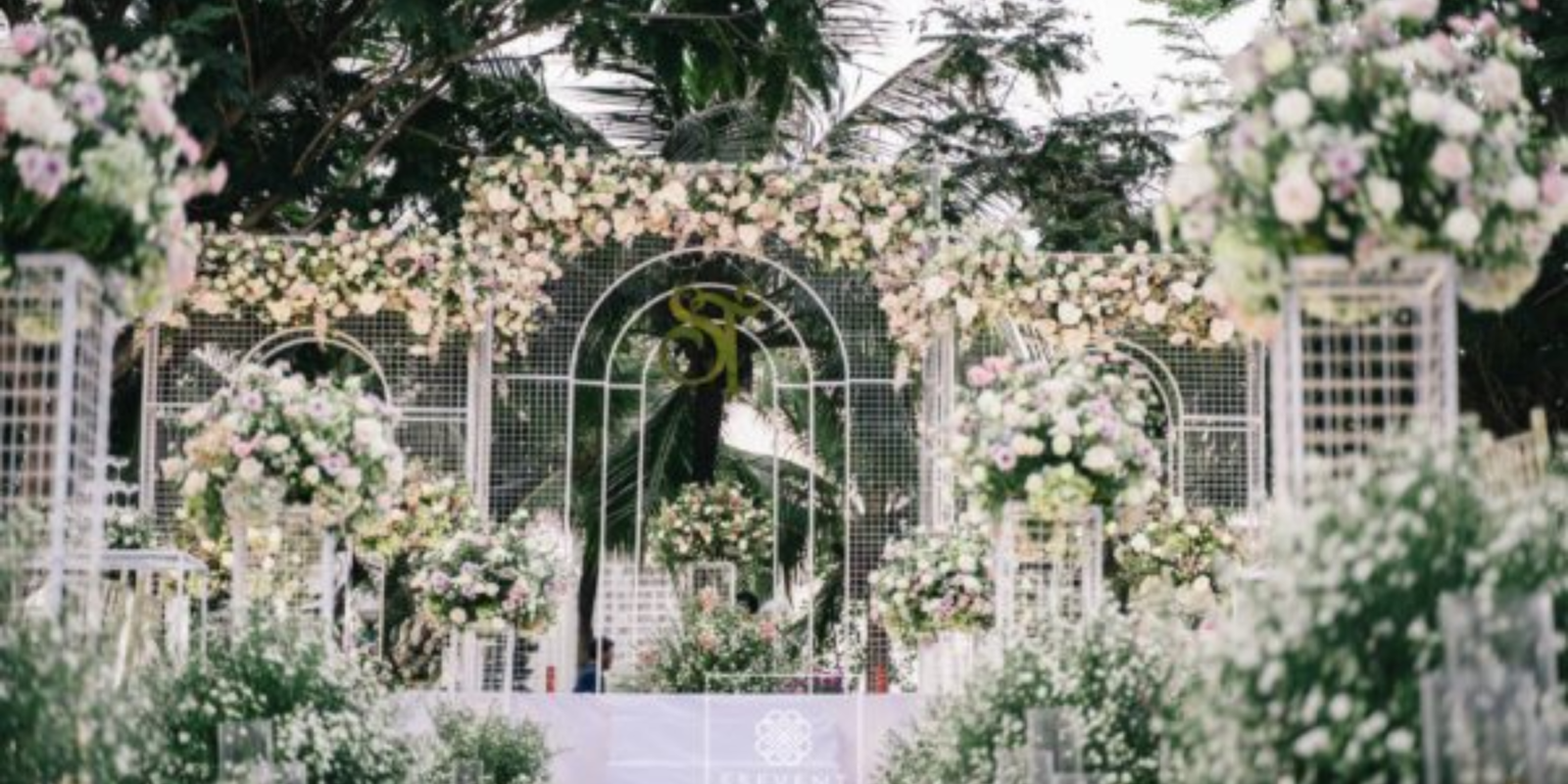 Backdrop Đám Cưới Ngoài Trời Phong Cách Châu Âu Đẹp Xuất Sắc  Một đám cưới ngoài trời luôn mang đến cảm giác lãng mạn, tự do và đầy cảm xúc. Khi không gian thiên nhiên được kết hợp cùng nghệ thuật trang trí tinh tế, buổi lễ cưới trở thành một khung cảnh như bước ra từ câu chuyện cổ tích. Trong đó, backdrop đám cưới ngoài trời chính là chi tiết quan trọng tạo nên linh hồn của toàn bộ không gian lễ cưới.  Nếu sân khấu là nơi cô dâu chú rể thực hiện những nghi thức thiêng liêng, thì backdrop đám cưới ngoài trời chính là phông nền giúp khoảnh khắc ấy trở nên hoàn hảo hơn. Một thiết kế đẹp không chỉ tạo điểm nhấn nổi bật cho buổi lễ mà còn giúp mọi bức ảnh cưới trở nên sang trọng và đầy cảm xúc.  Trong những năm gần đây, xu hướng backdrop đám cưới ngoài trời phong cách châu Âu đang được nhiều cặp đôi yêu thích. Phong cách này mang đến vẻ đẹp tinh tế, thanh lịch nhưng vẫn rất lãng mạn. Những chi tiết như hoa tươi, khung vòm, rèm lụa mềm mại hay ánh đèn vàng ấm áp giúp không gian lễ cưới trở nên nhẹ nhàng và đầy cảm